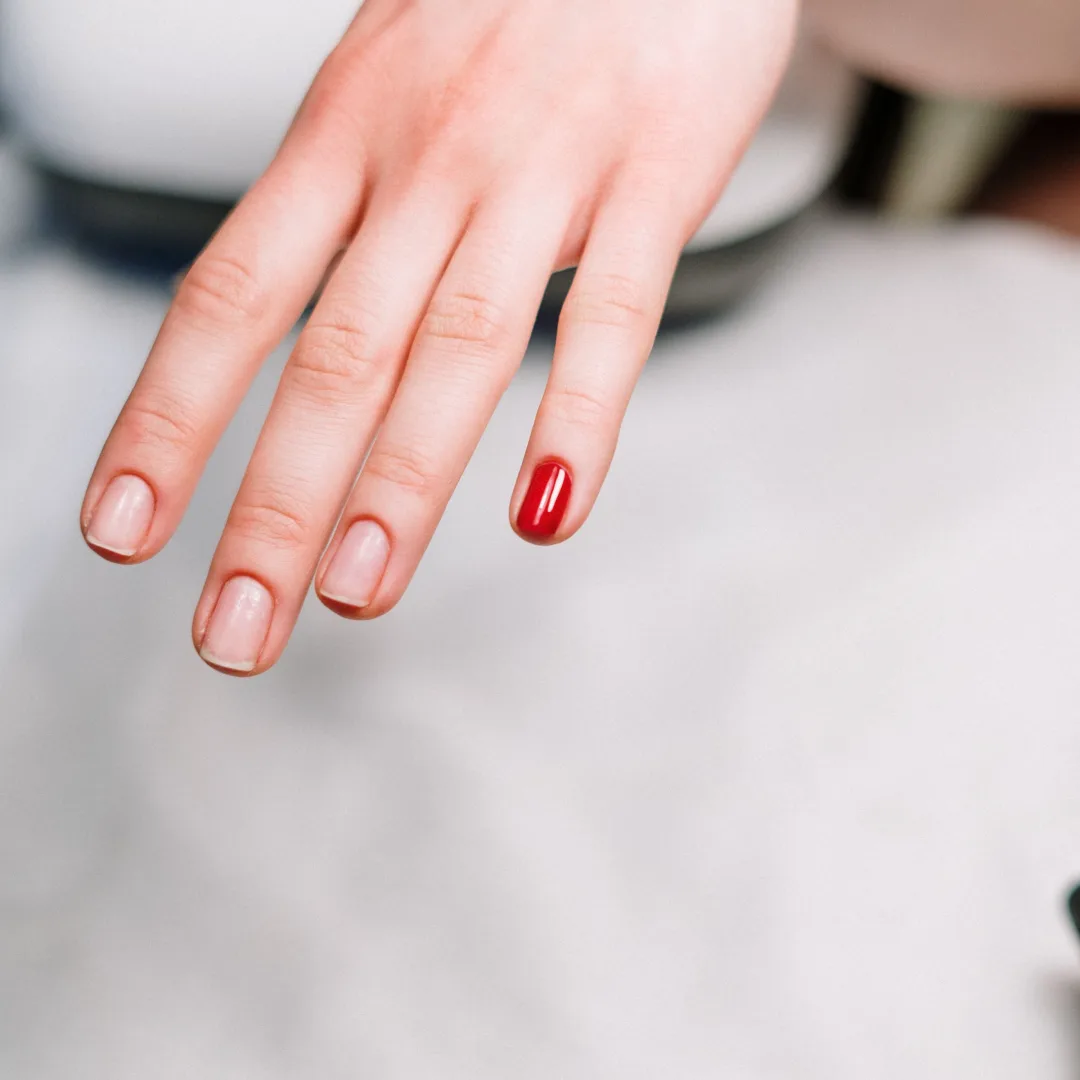 A close-up of a hand with one red painted nail, showcasing a minimalistic manicure style.