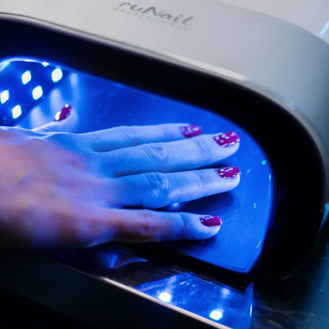A hand with red nail art curing under a UV lamp in a professional nail salon.