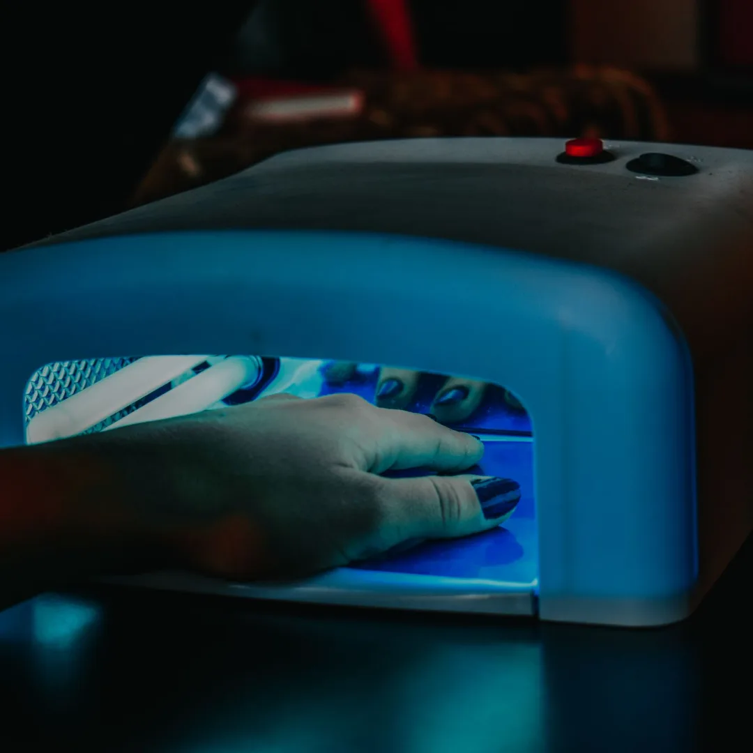A hand with manicured nails being cured under a blue LED lamp for gel polish.